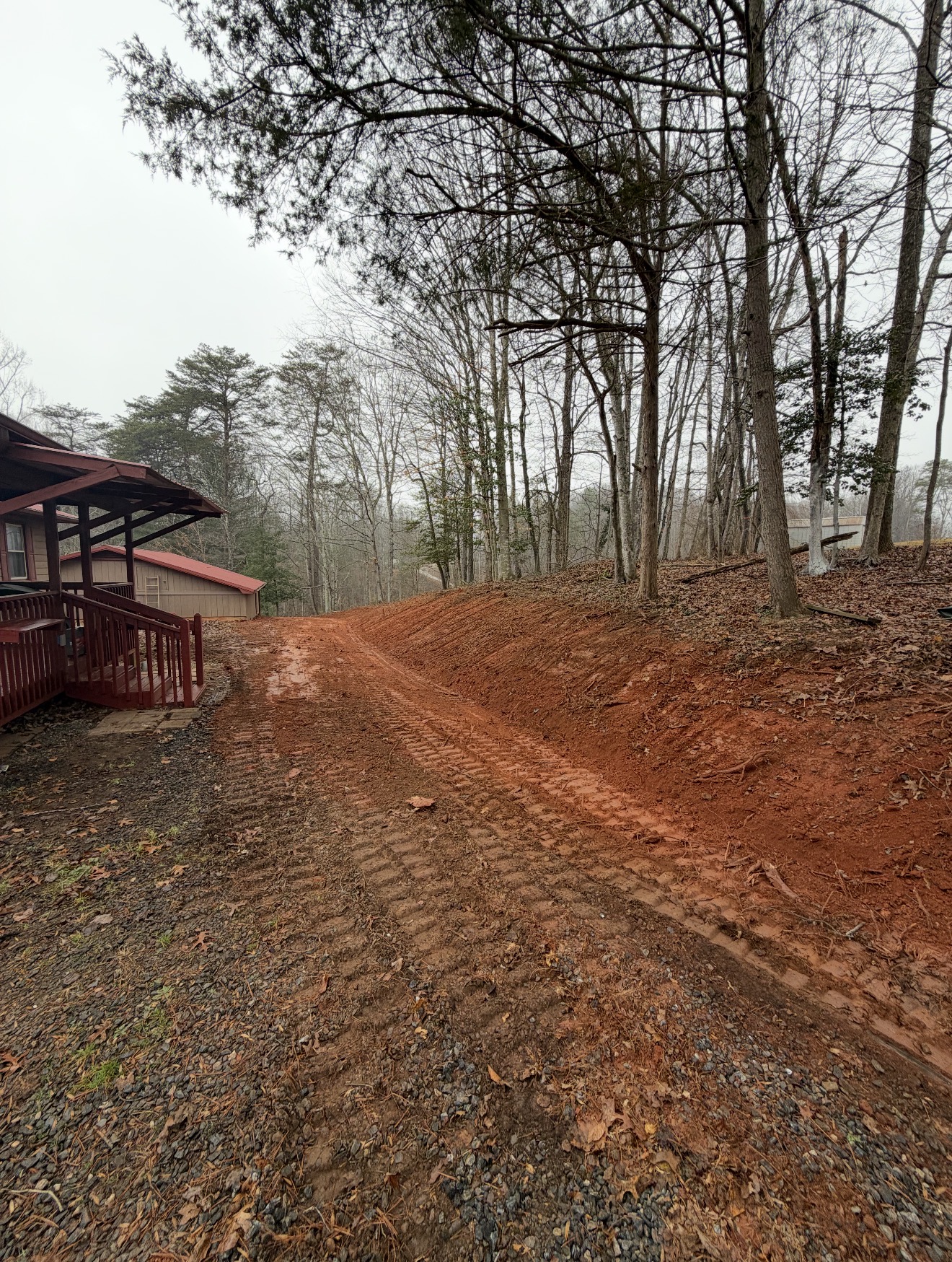 Graded red clay driveway with drainage swale next to a residential cabin